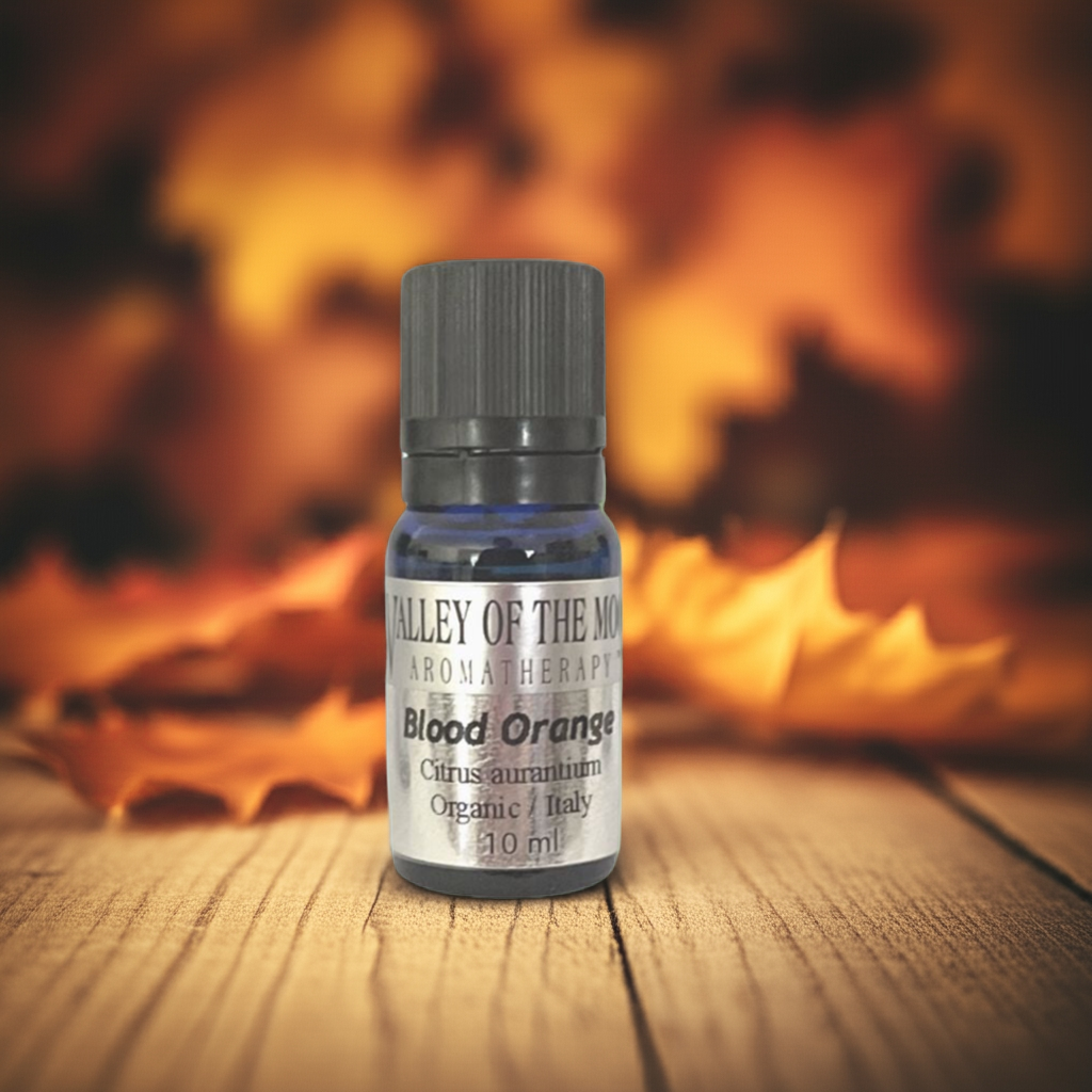 Bottle of Valley of the Moon Aromatherapy Blood Orange essential oil on a wooden surface with autumn leaves in the background.
