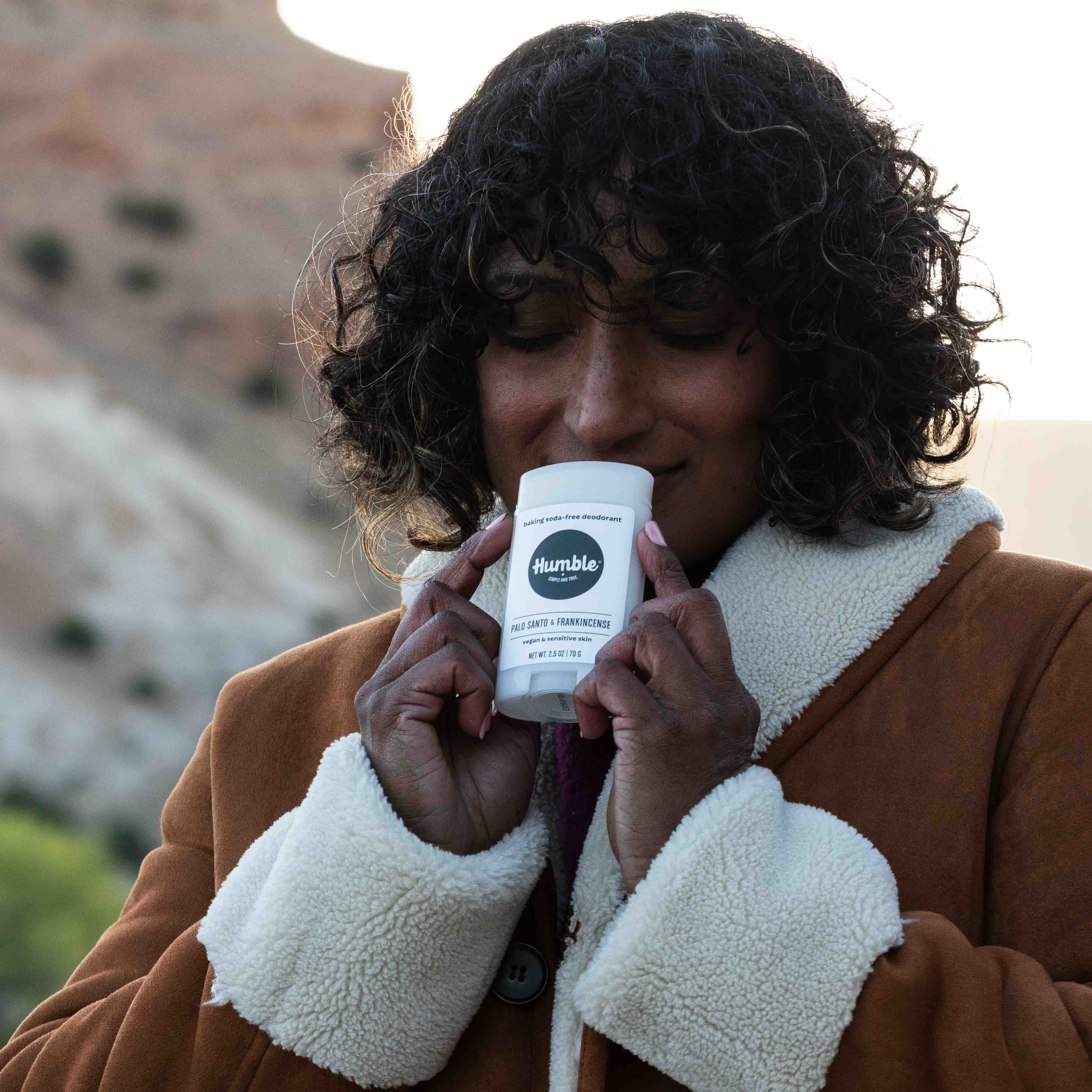 Woman outdoors smelling and holding Humble vegan deodorant – Palo Santo & Frankincense scent for sensitive skin – natural, baking soda free – www.aromathyme.com