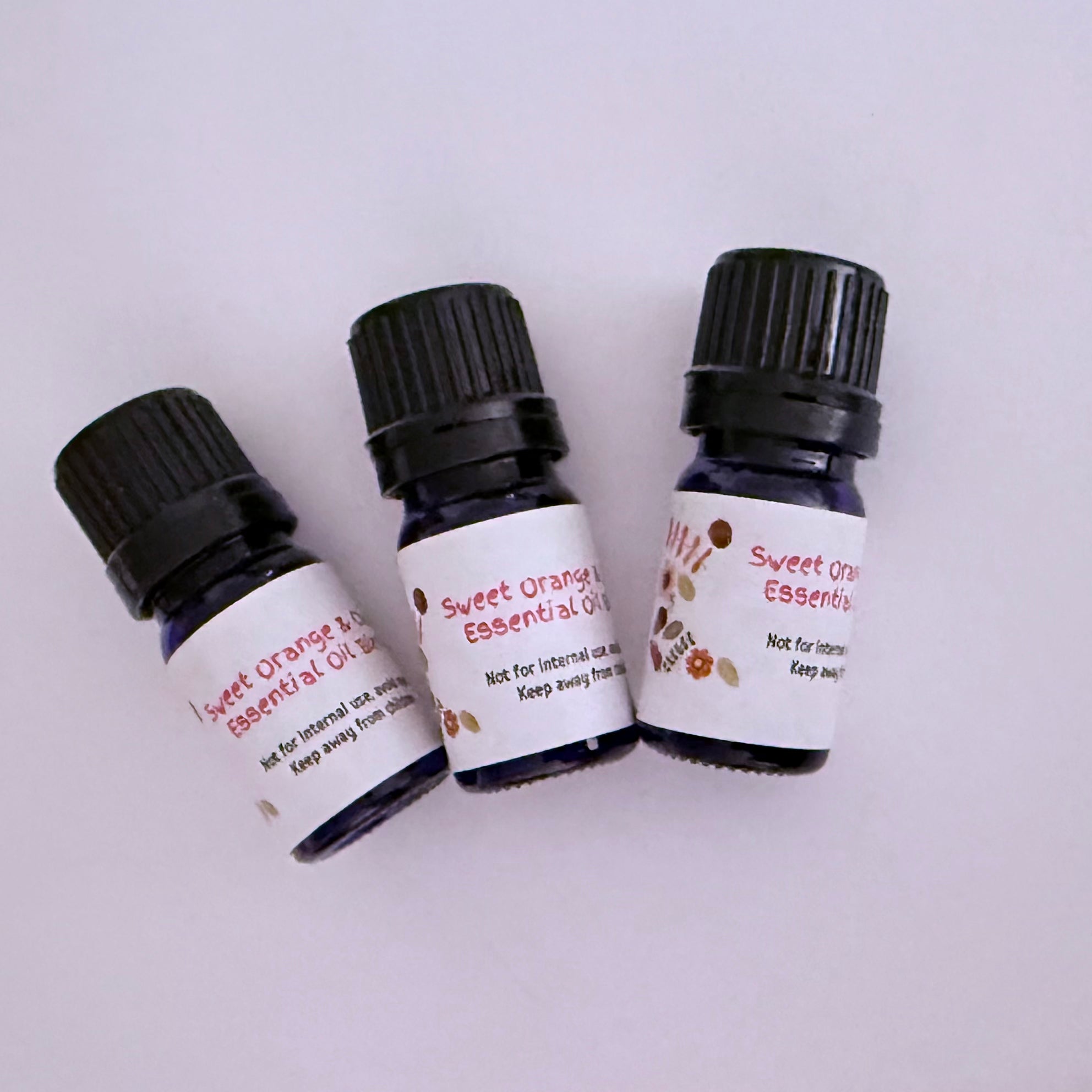 Three bottles of Sweet Orange and Clove Essential Oil Blend by Aroma Thyme with black caps on a white background
