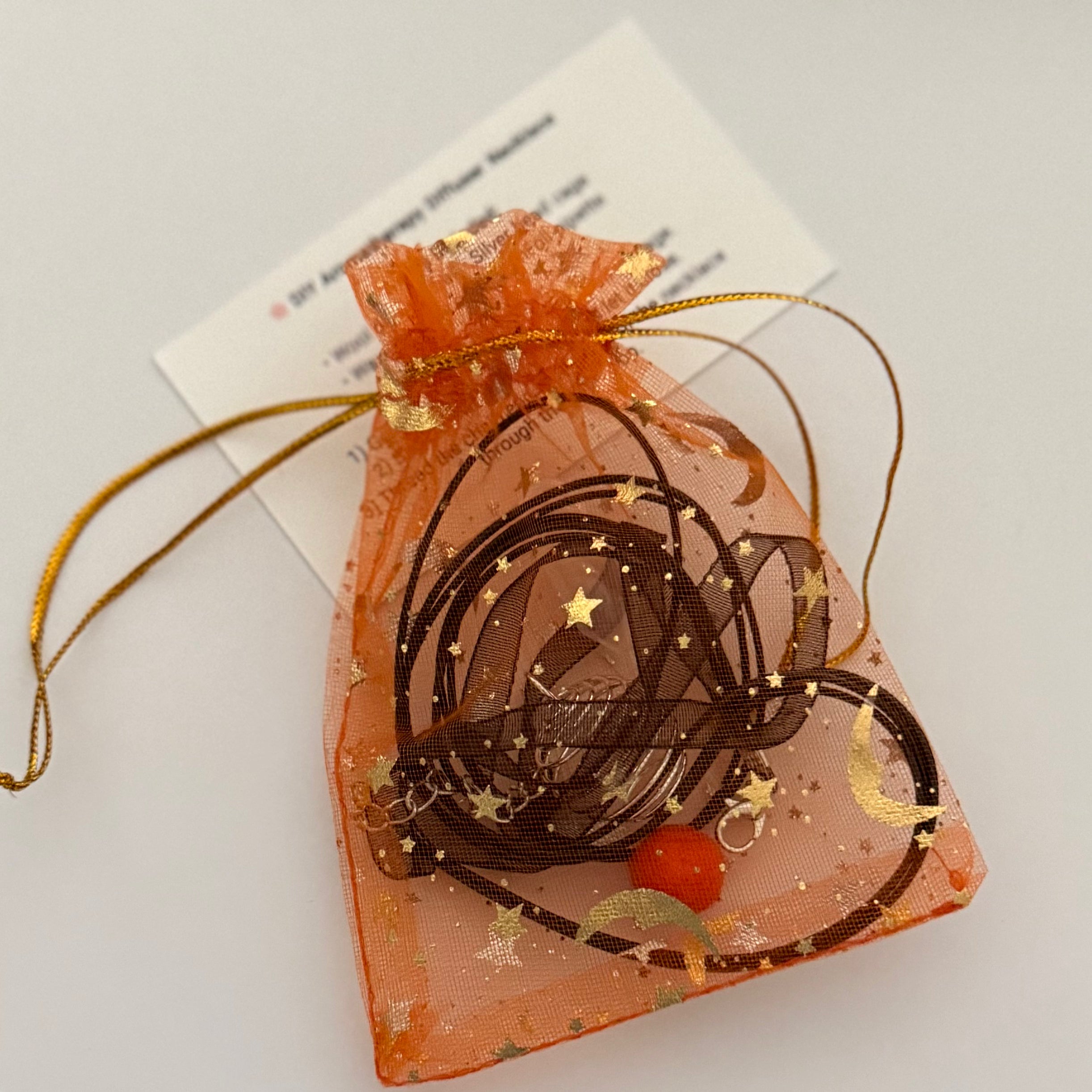 DIY aromatherapy necklace kit in an orange drawstring bag on a light gray background