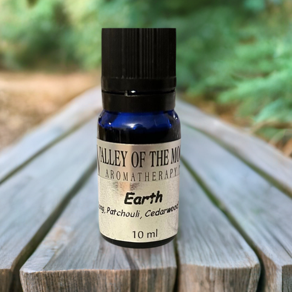 Aromatherapy essential oil bottle labeled 'Earth' by Valley of the Moon Aromatherapy on a wooden surface with a natural background.