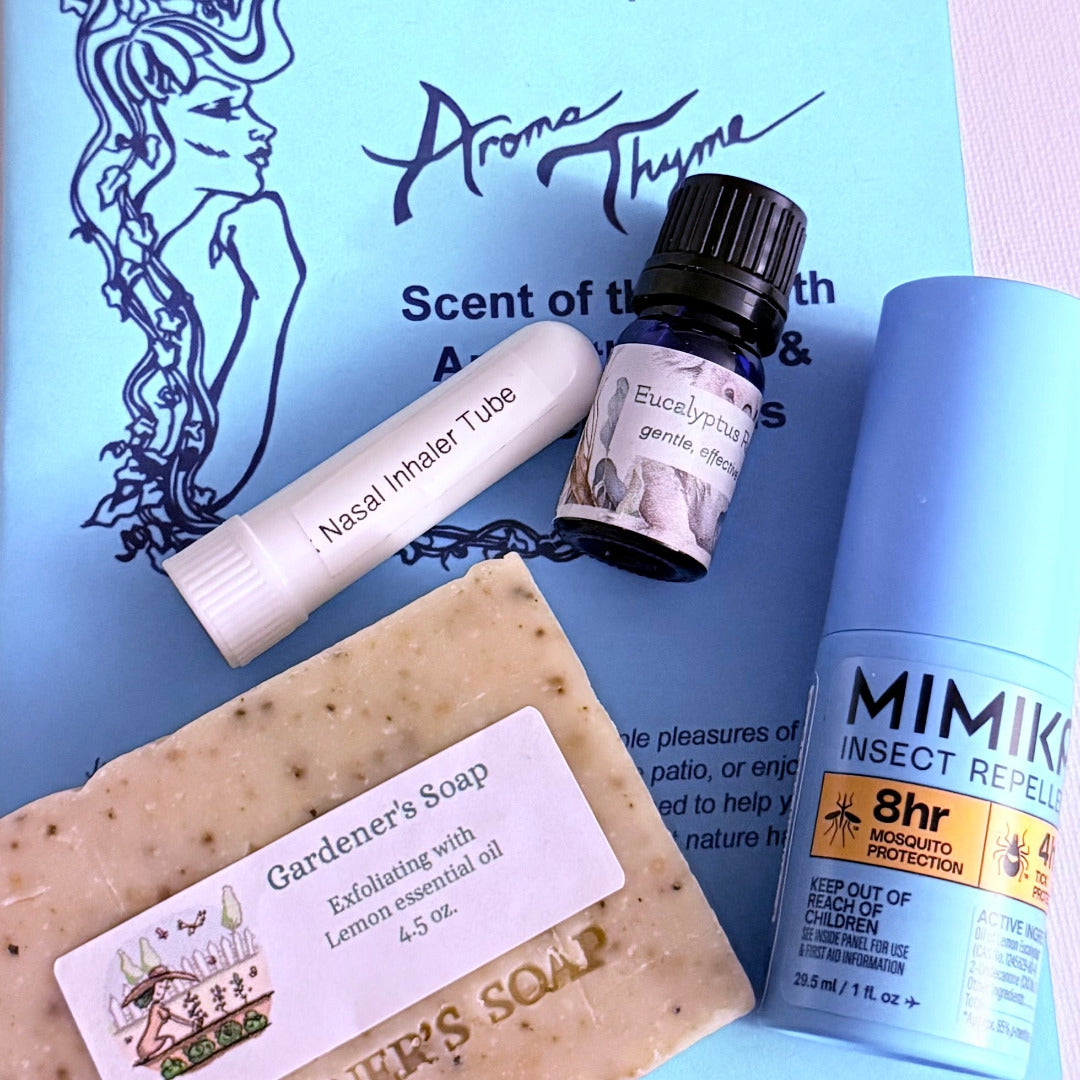 A flat-lay arrangement of several personal care products on a light blue printed card: a bar of speckled soap labeled Gardener's Soap, a white nasal inhaler tube, a small dark bottle labeled Eucalyptus, and a light blue Mimik insect repellent can.
