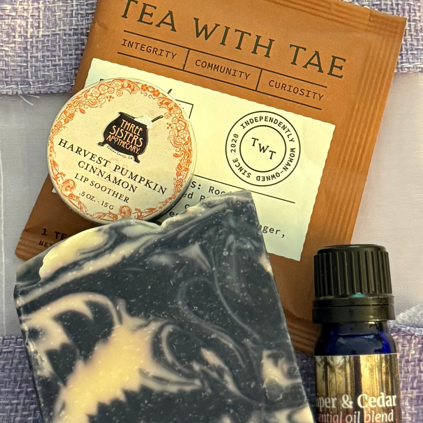 Aroma Thyme Scent of the Month Club seasonal box with pumpkin lip balm, soap, juniper cedar oil blend and brown package of tea on a purple background.