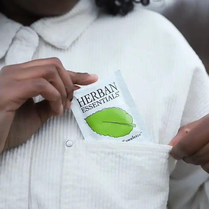 Person holding a Herban Essentials product package with a leaf logo.