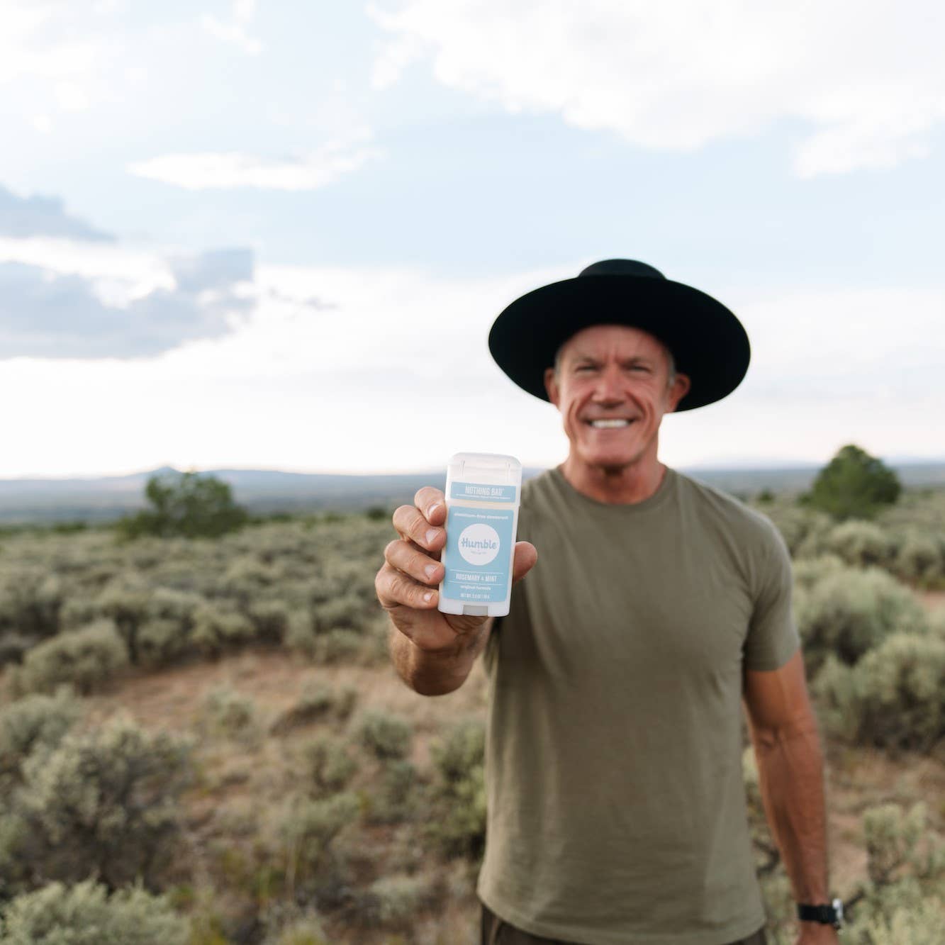 Man outdoors holding Humble original formula deodorant – Rosemary & Mint  scent, aluminum free -available at www.aromathyme.com 